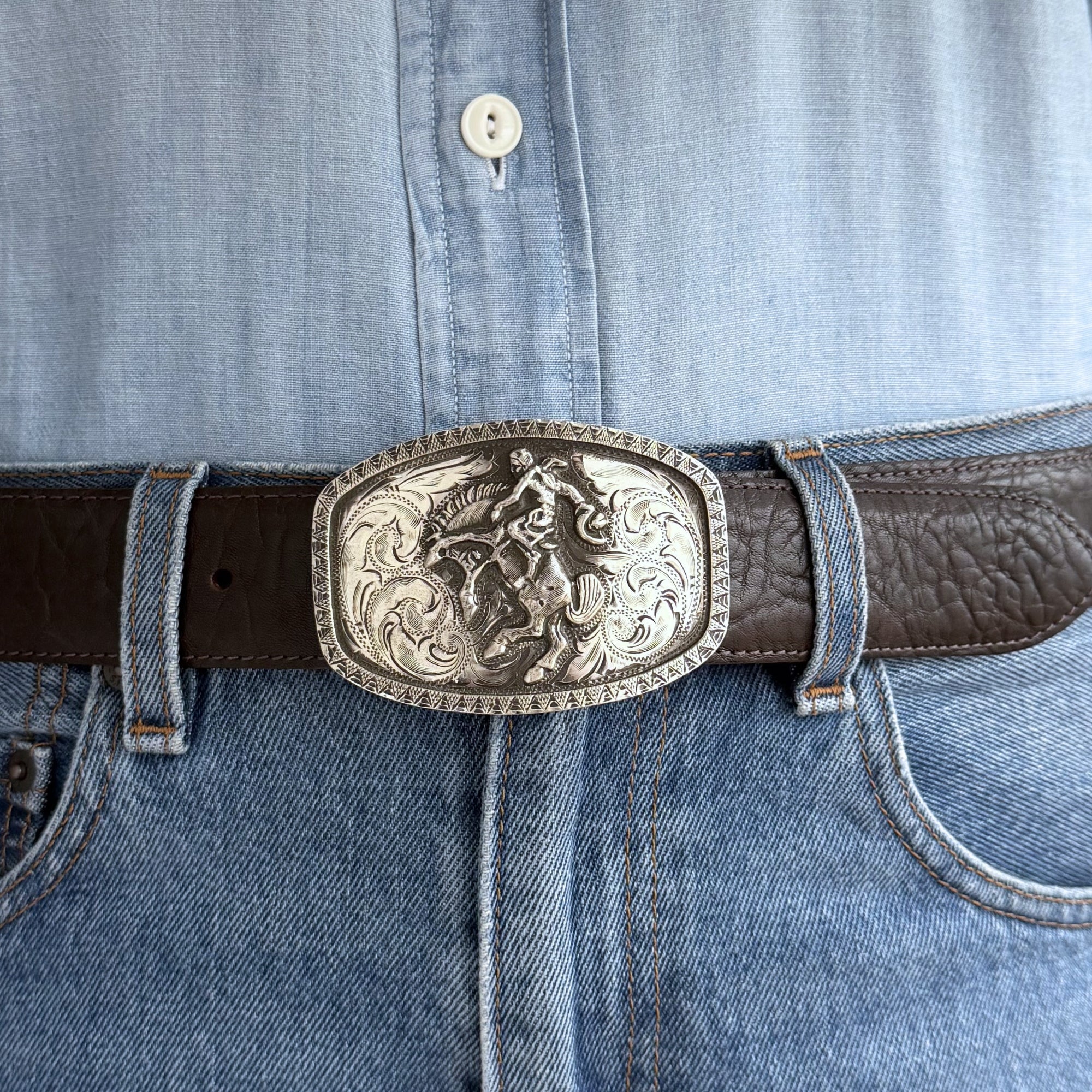Oval Silver buckle with bronc rider and raised border on belt