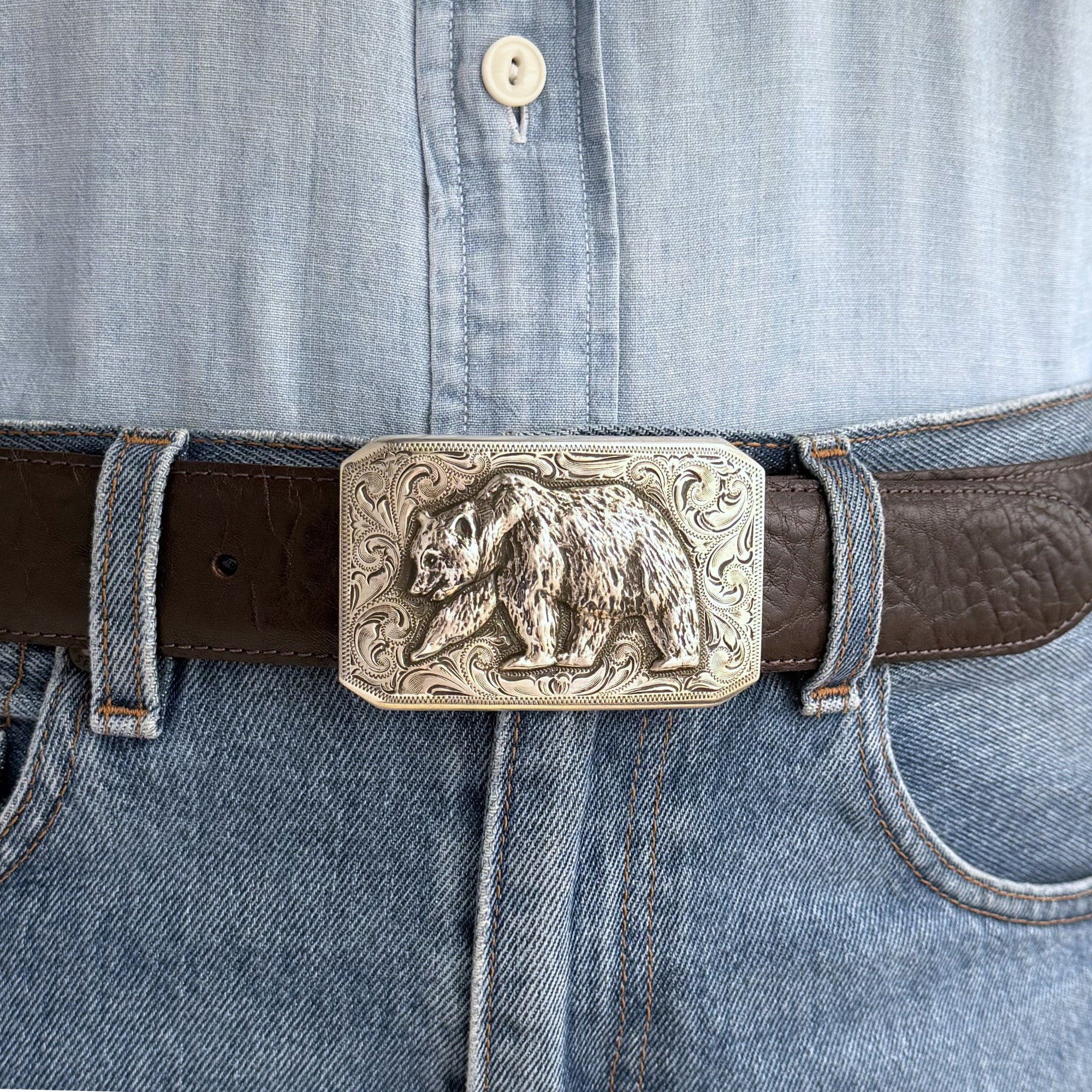 close up of rectangular silver Bohlin buckle with an overlaid bear and engrave background.