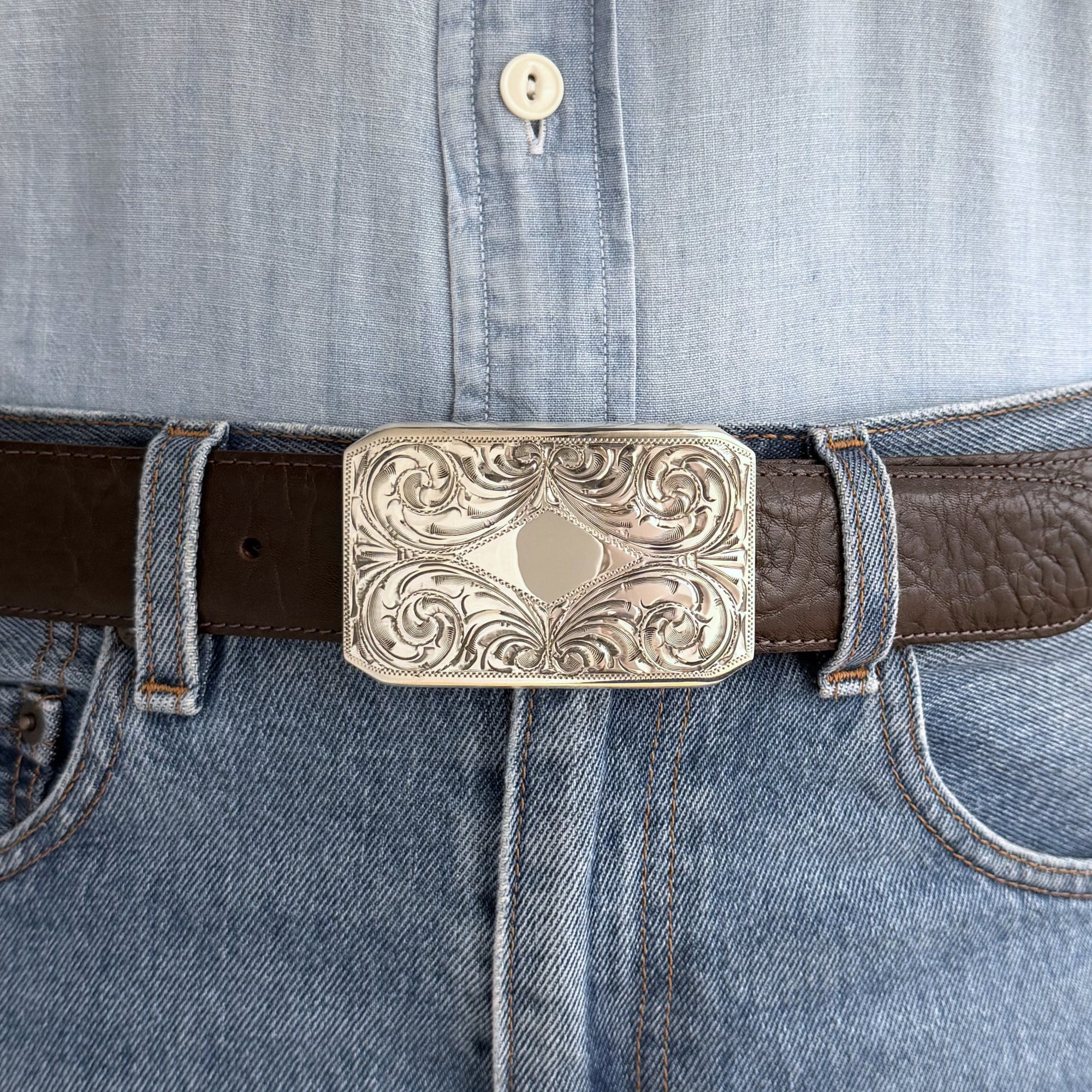 Close-up of a belt with an ornate buckle on a denim shirt.