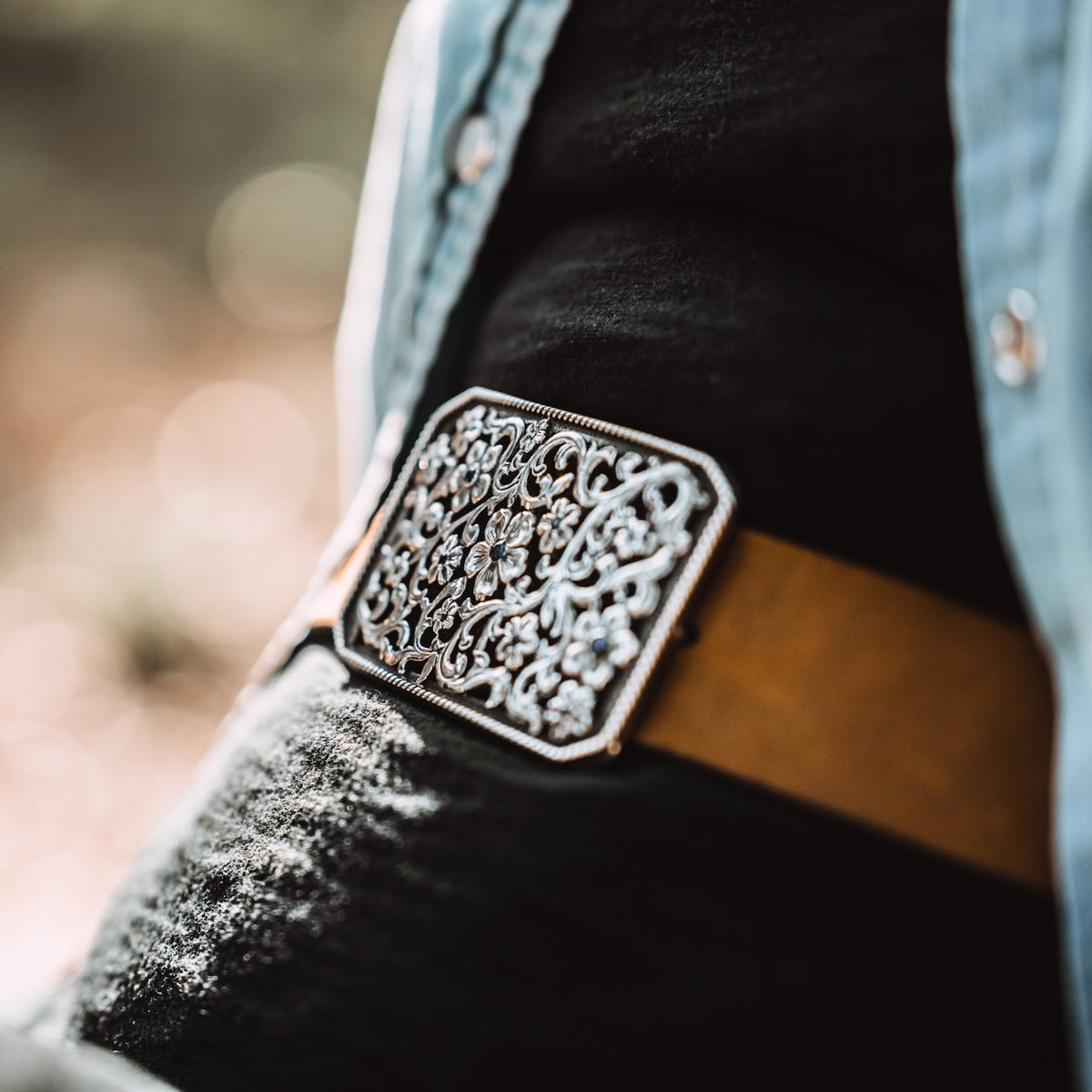 Rectangle hand fabricated Bohlin buckle with set sapphires in a full filigree flowers and scrolls silver buckle on brown belt. 
