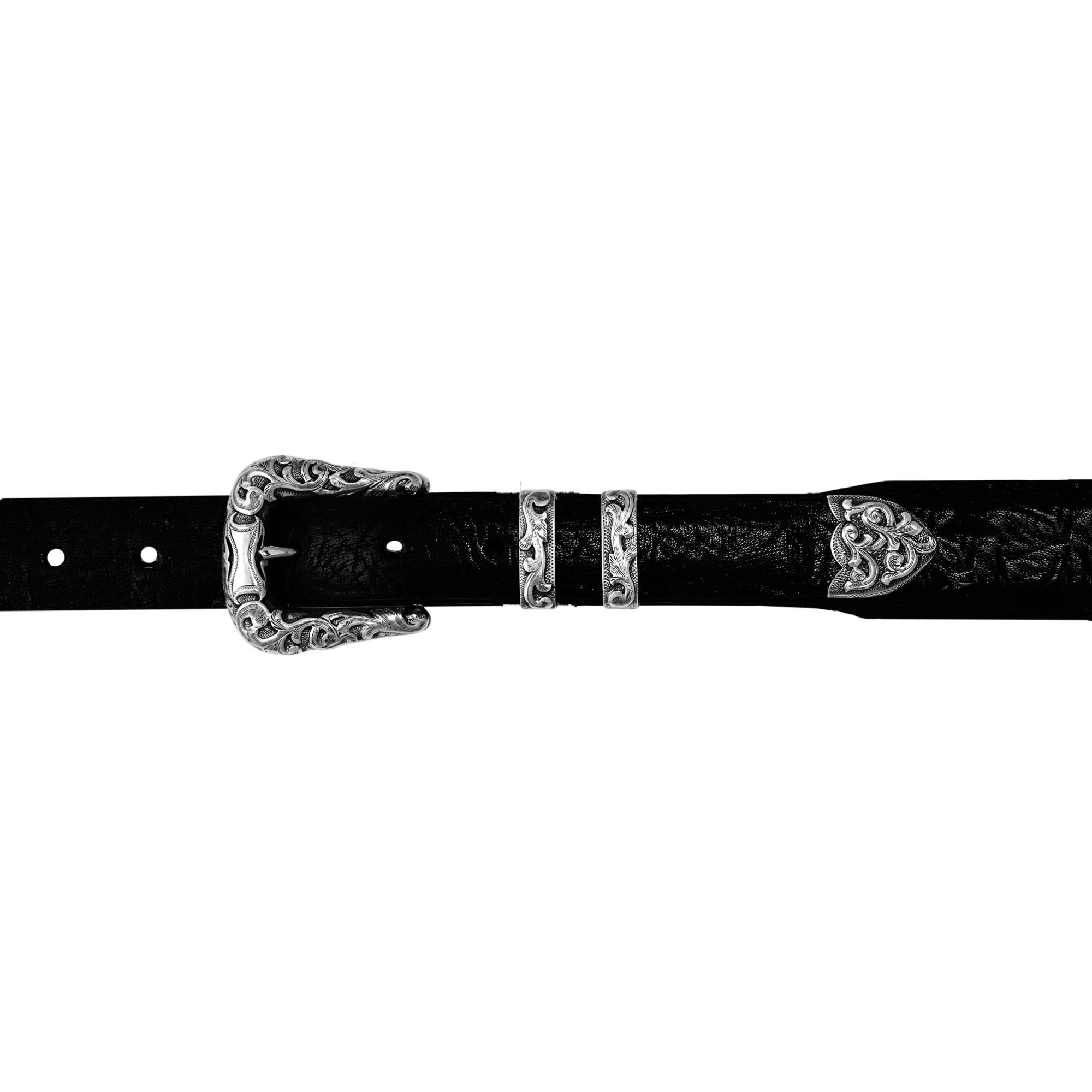 A black textured leather belt with ornate hand-cut filigree scrolls surrounding a raised shield overlay buckle, keeper, and tip, shown against a plain white background.