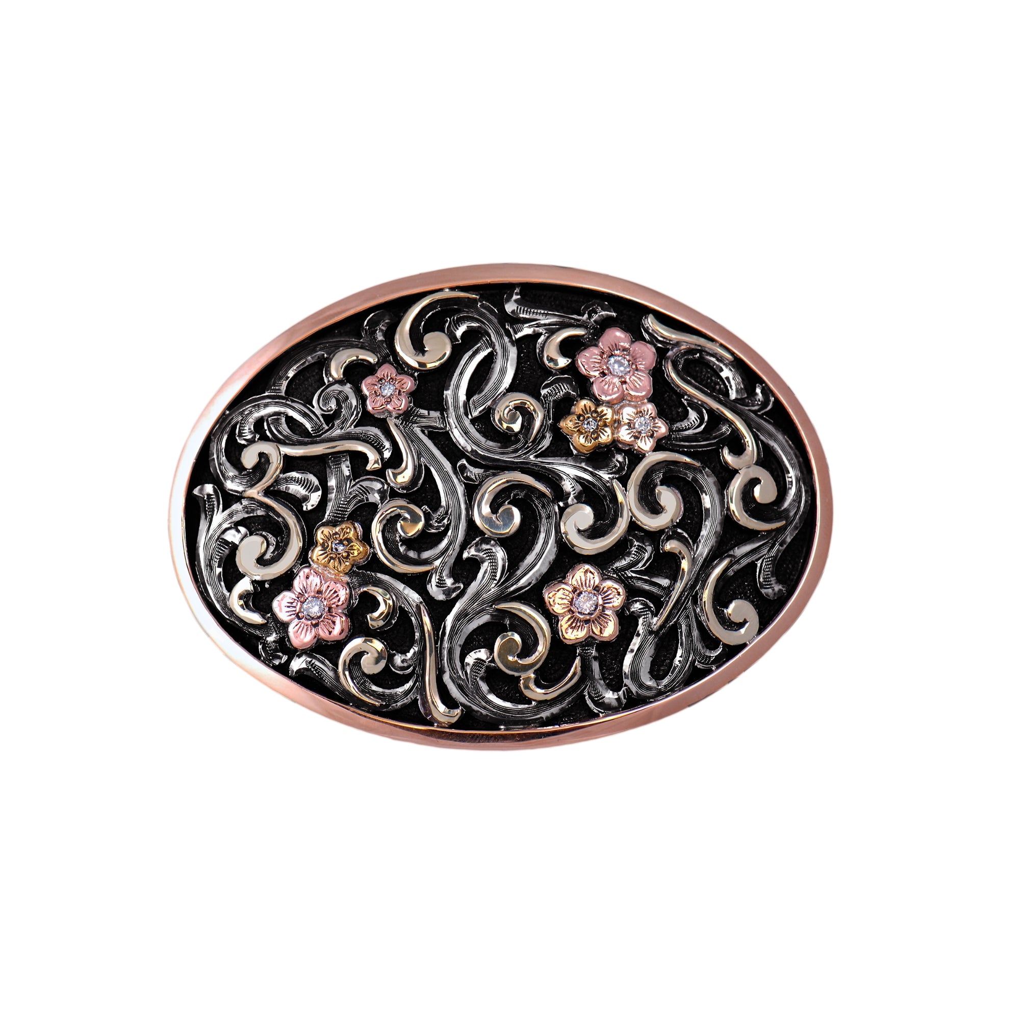 An oval belt buckle featuring an ornate filigree scrollwork design in black and rose gold, accented with three small pink and gold floral motifs, set against a plain white background.
